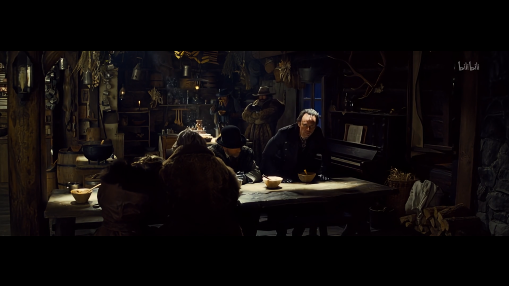 A film still of people arranged around a cabin interior, illustrating staging that a game must also make interactive.